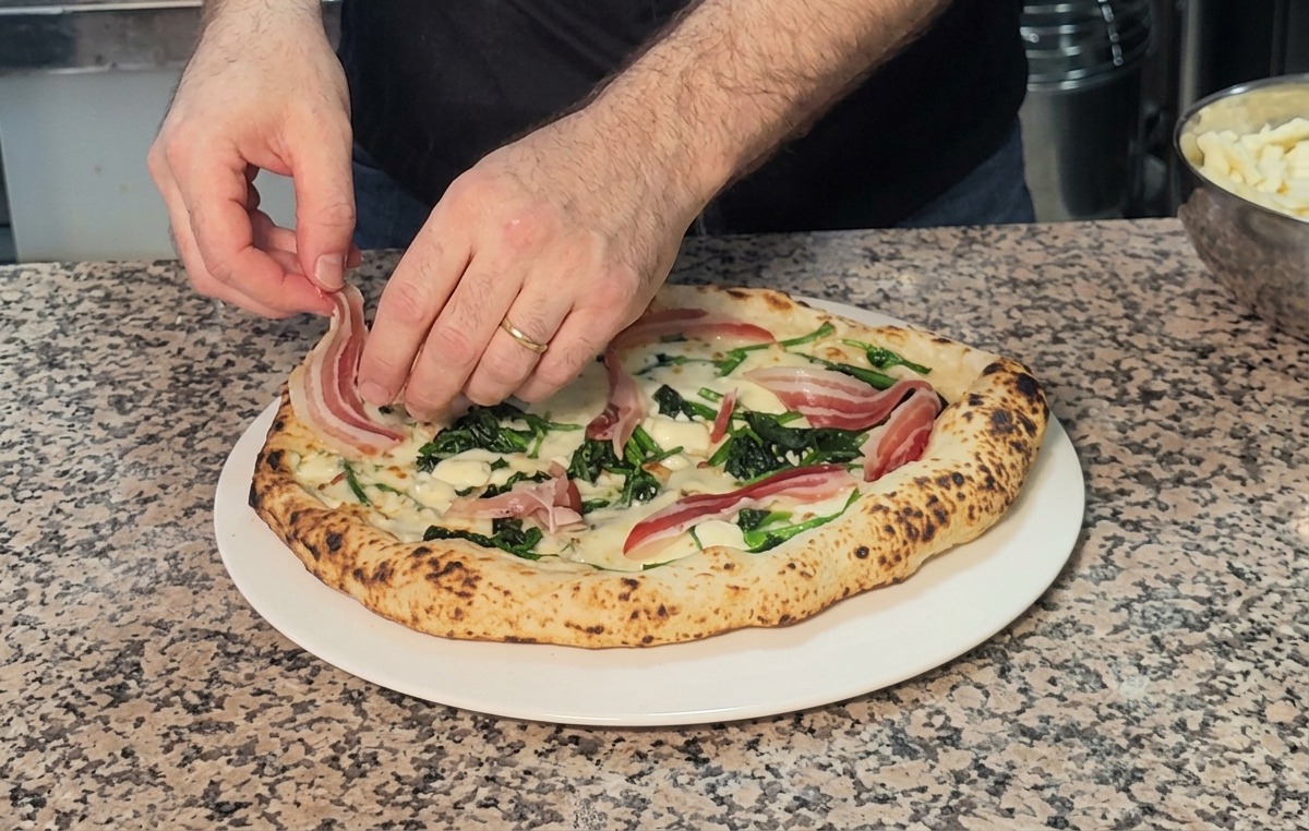 Draping thin slices of pancetta over a freshly baked hot spinach and cheese pizza.