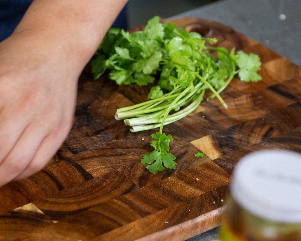 Fresh cilantro leaves and stems resting on a wooden cutting board, ready to be chopped by hand.
