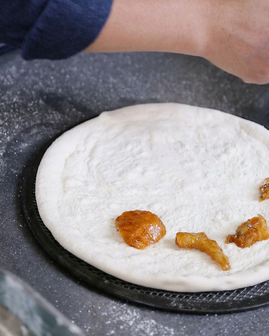 A hand placing marinated pieces of raw seafood directly onto a stretched white pizza dough.