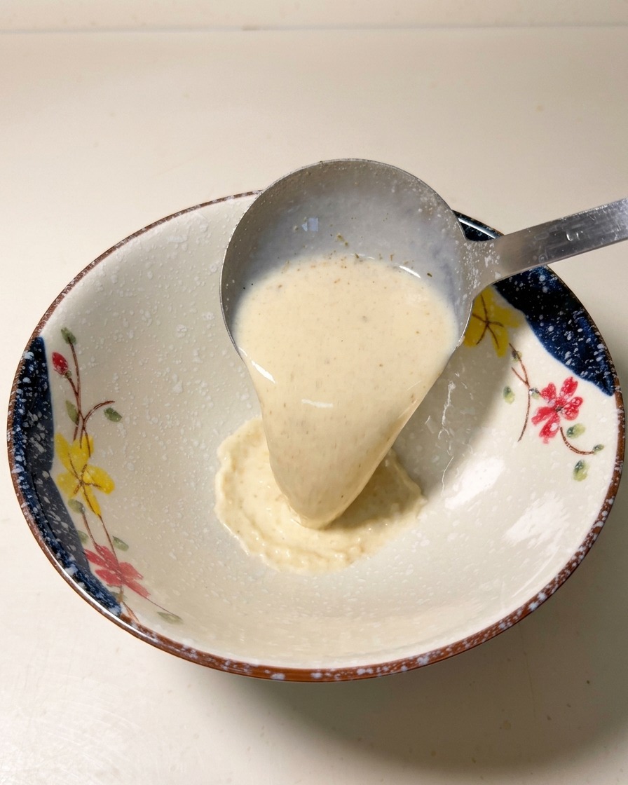A metal ladle pouring hot, creamy ramen soup base into a patterned ceramic bowl.