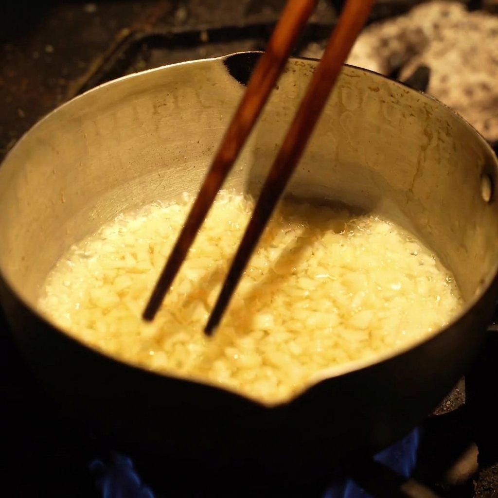 Small chunks of garlic frying and bubbling vigorously in hot oil inside a metal pot.