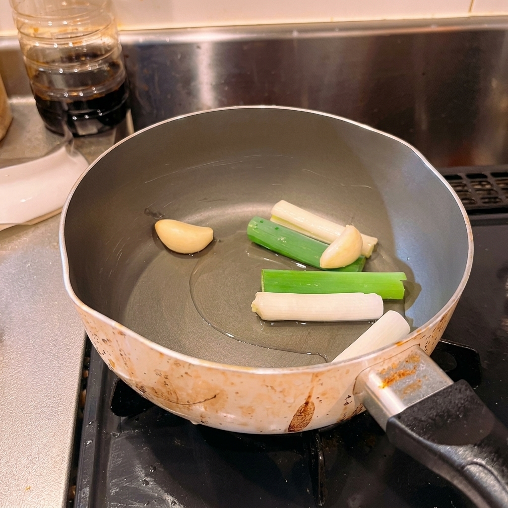 Chopped scallions and whole garlic cloves sitting in a small pool of cold oil inside a cooking pot.