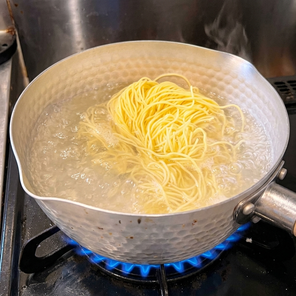 A bundle of fresh yellow ramen noodles sitting in a silver pot of bubbling, boiling water.