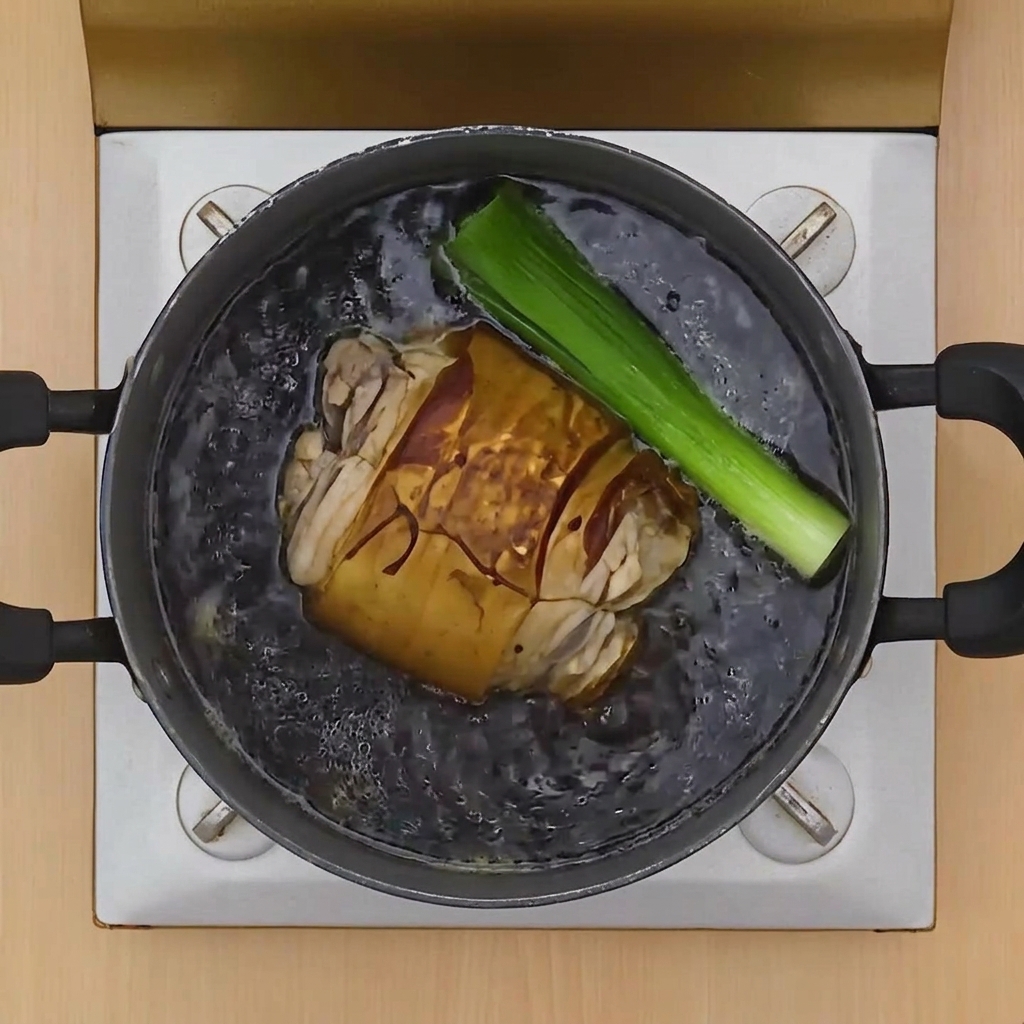 A browned pork belly roll simmering in a dark soy-based broth alongside a large piece of green onion.