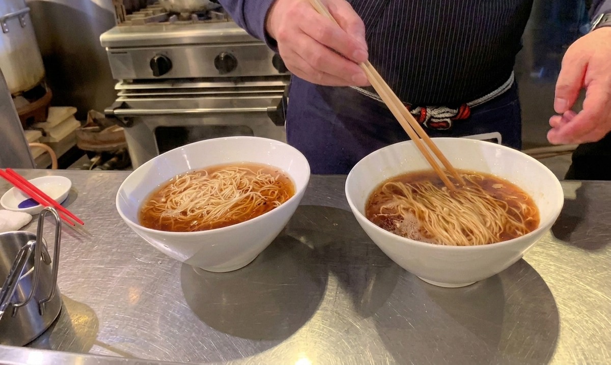 Using long wooden chopsticks to neatly fold and arrange ramen noodles perfectly inside the broth.