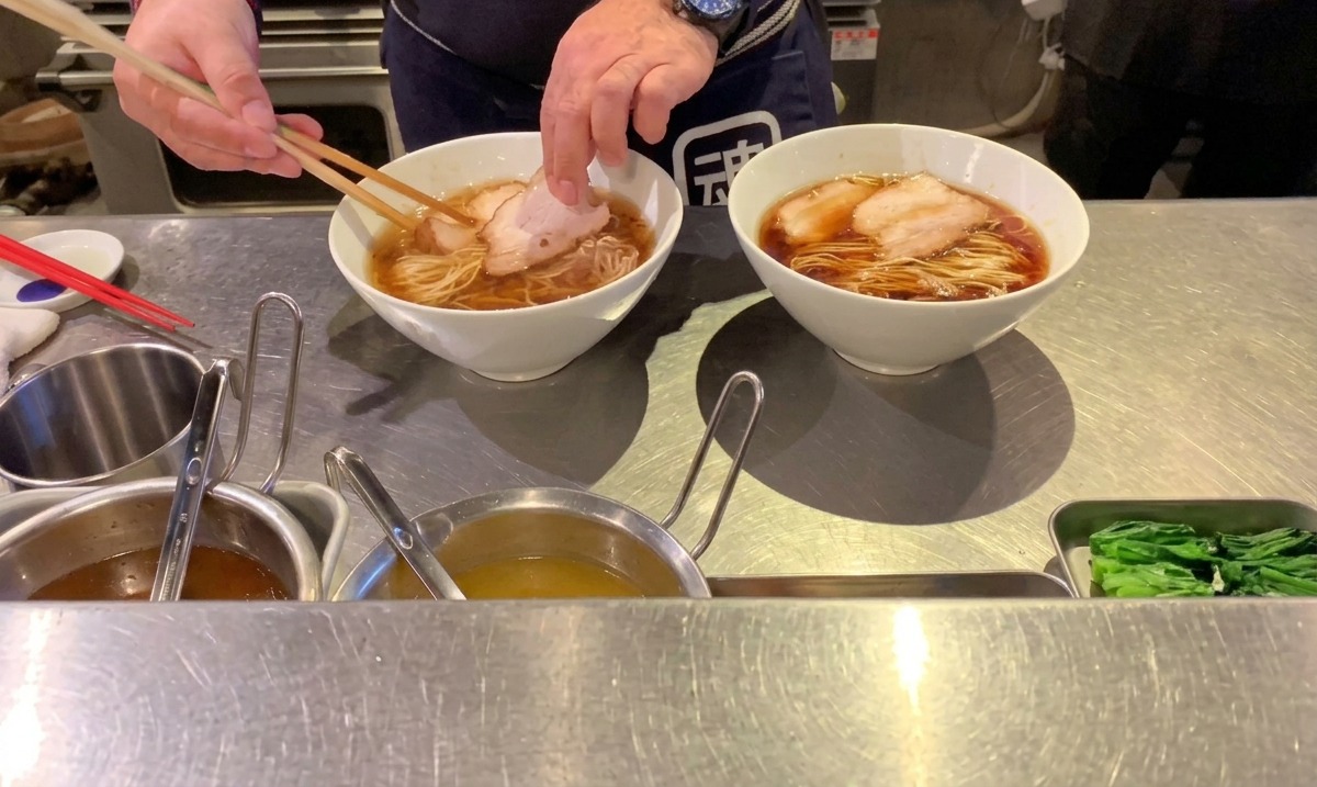 Chef placing slices of cooked pork chashu onto the arranged ramen noodles using chopsticks.