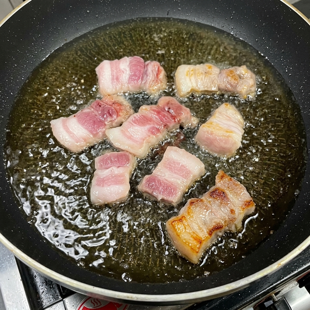 Thick cuts of pork belly pan-frying in a pool of oil, showing caramelized, golden-brown surfaces.