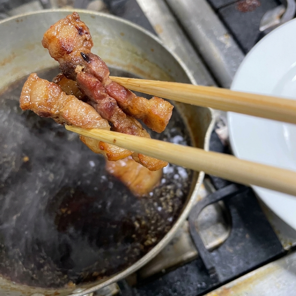 Chopsticks lifting pieces of braised dark pork belly out of a simmering pot of sauce.