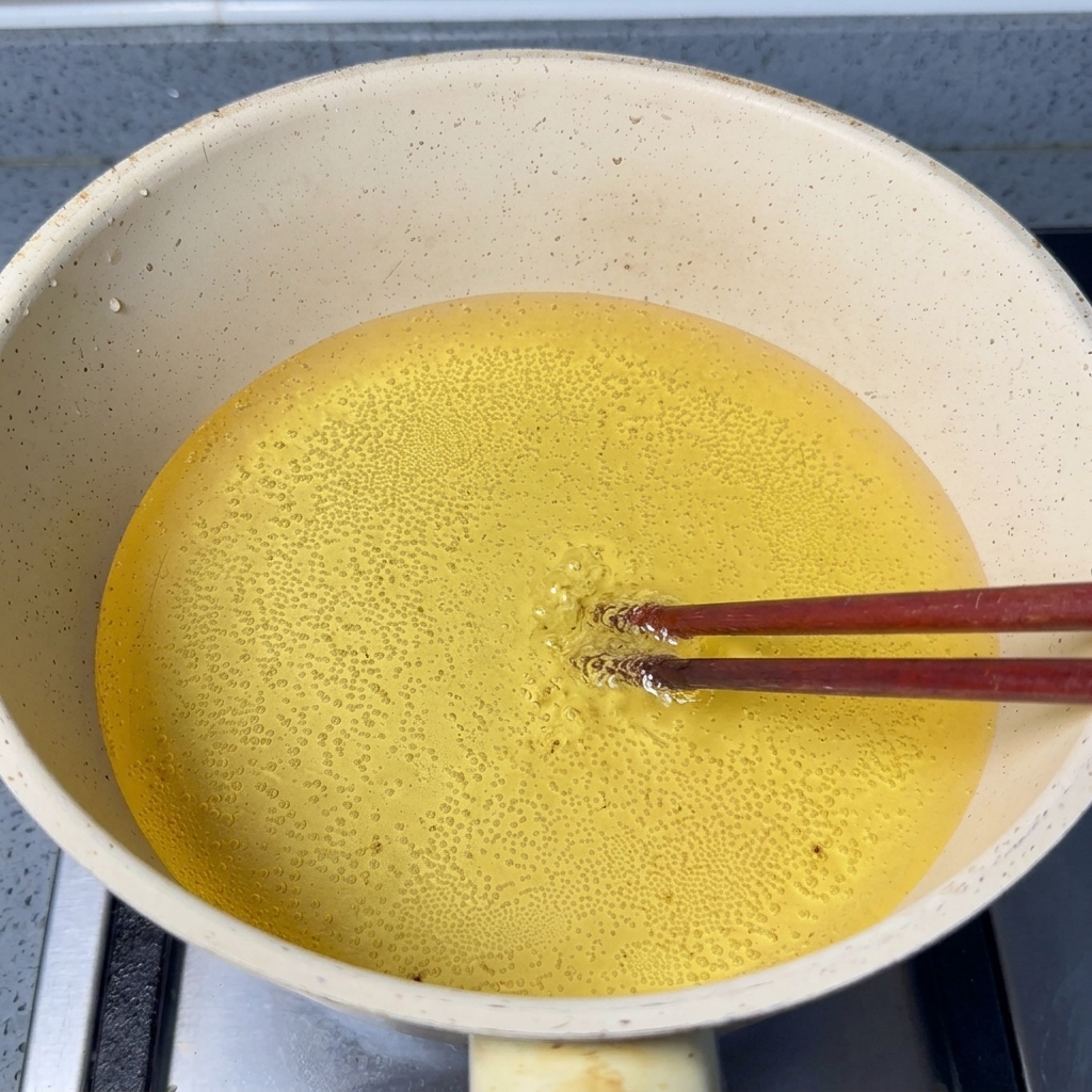 Wooden chopsticks submerged in hot oil with small bubbles actively forming around the tips.