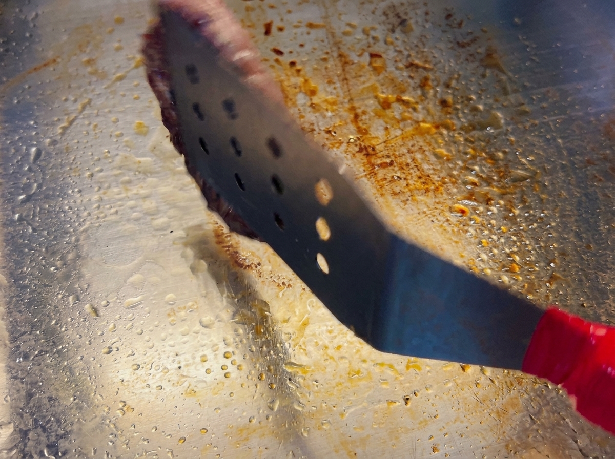 A metal spatula lifting a beef patty to flip it, showing a beautifully browned crust on the bottom side.