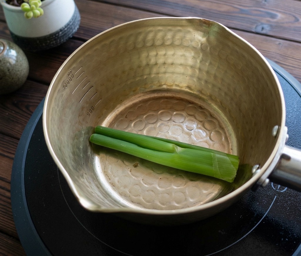 Whole green scallion stalks placed in the bottom of an empty golden metal pot.