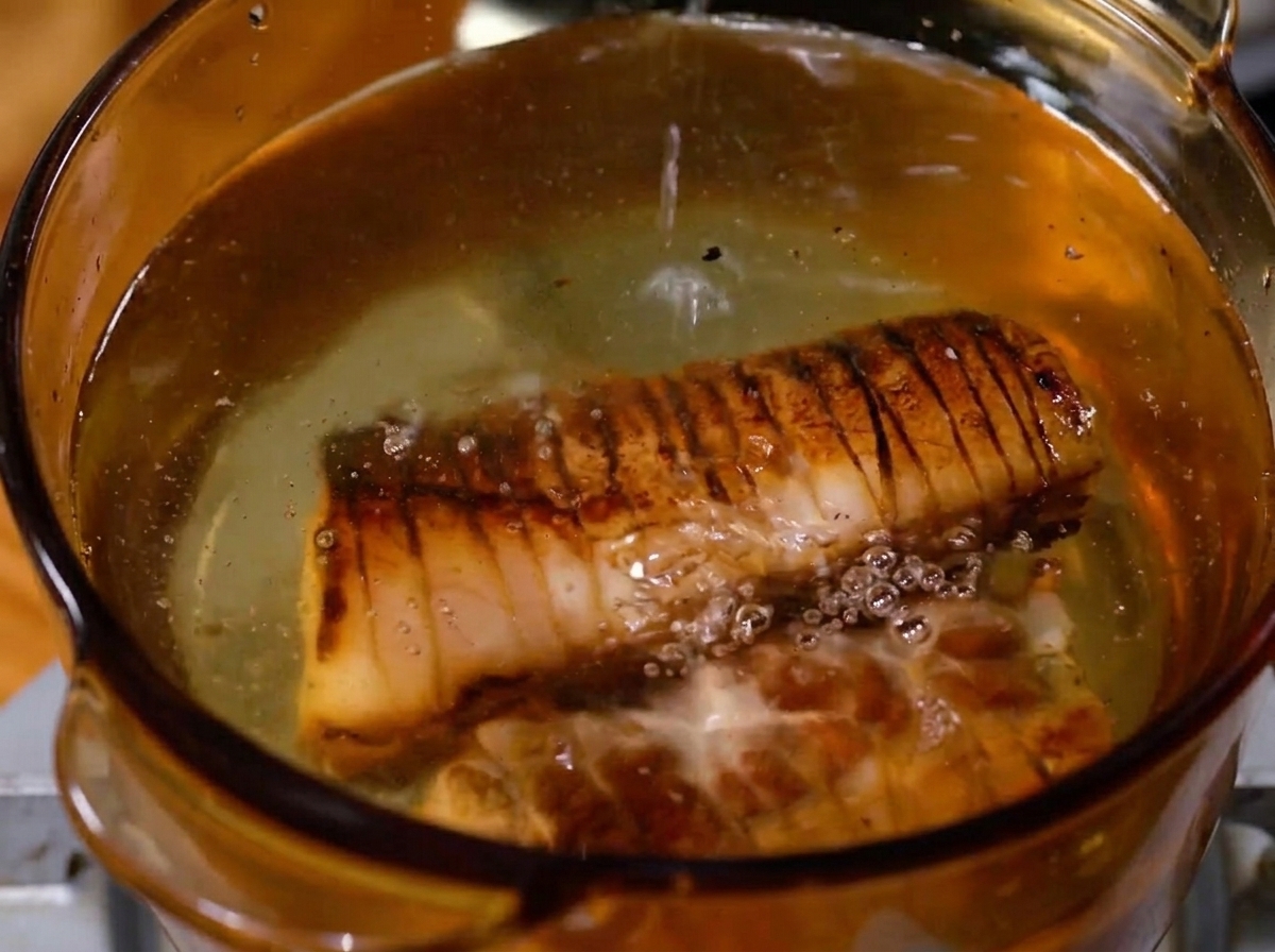 A tied piece of seared pork belly simmering in a pot of bubbling liquid.