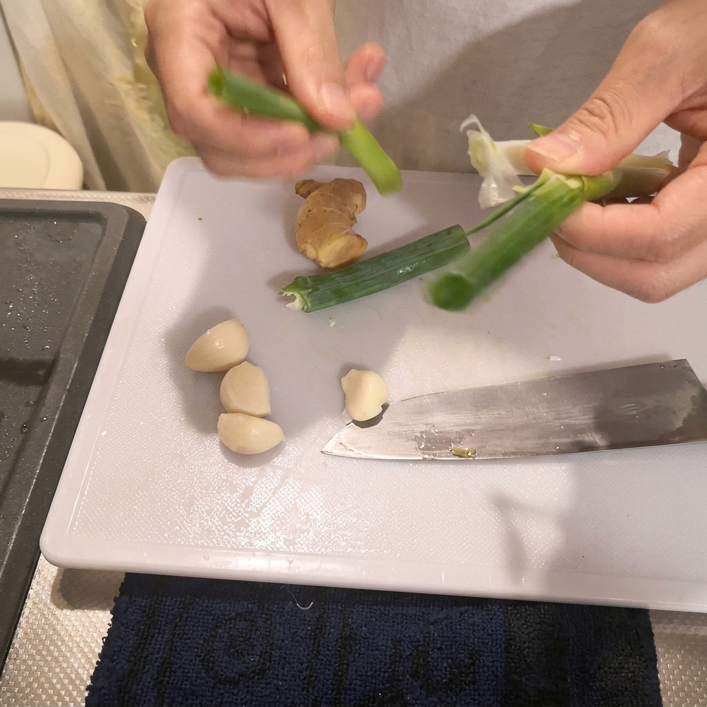 Hands preparing green scallions on a white cutting board next to a kitchen knife.