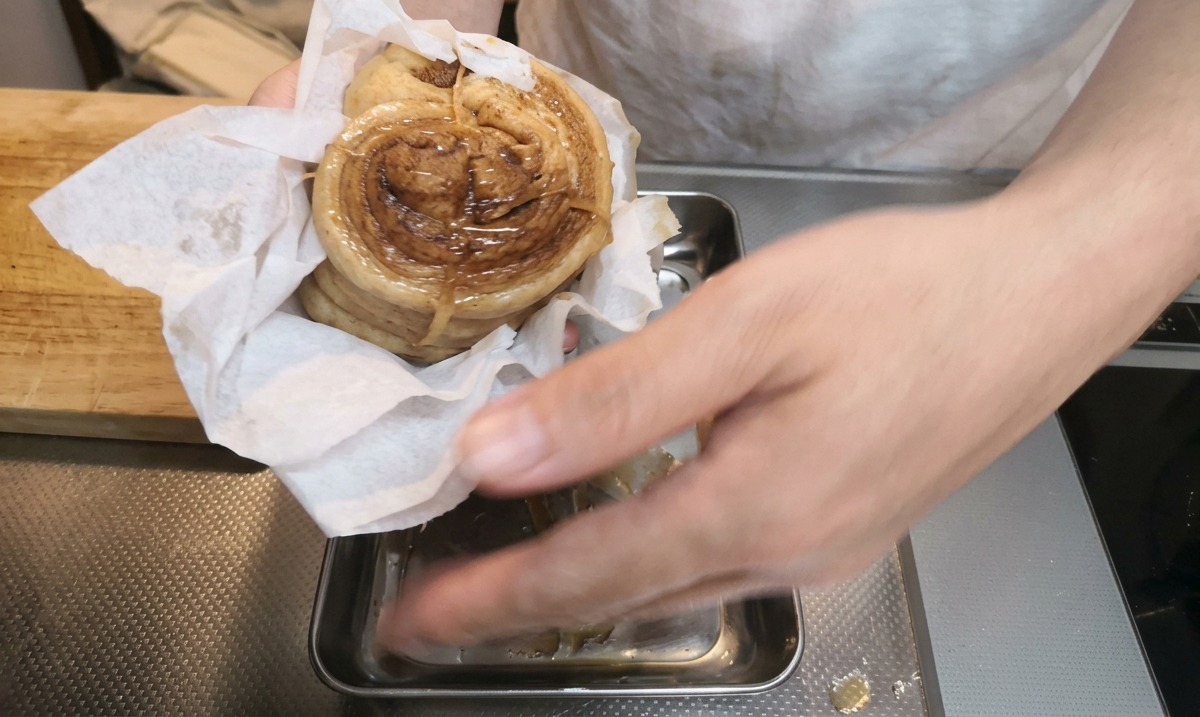 Hands using a paper towel to pat dry a braised pork belly roll over a metal tray.