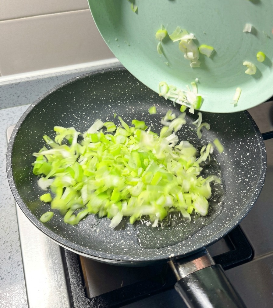 Chopped green onions being transferred from a light green plate into a hot frying pan.