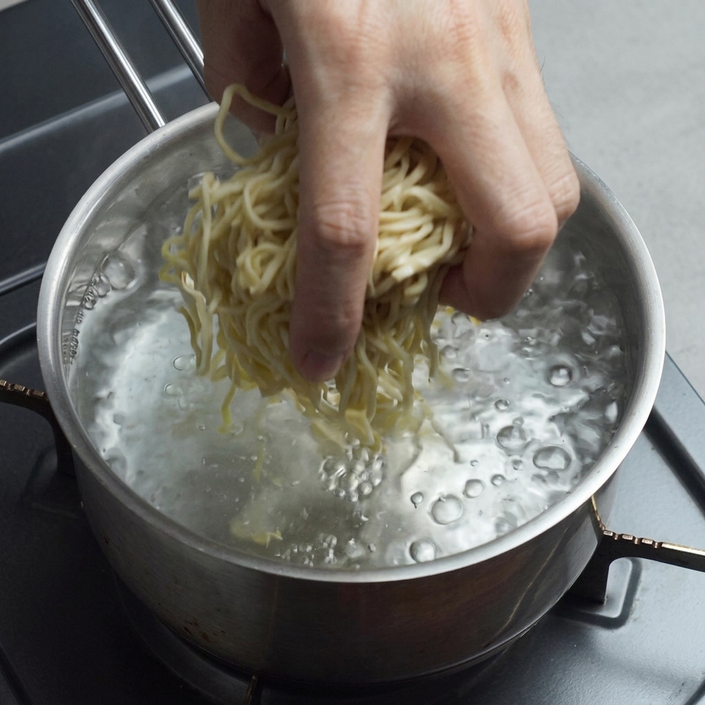 A hand dropping fresh yellow ramen noodles into a pot of vigorously boiling water.
