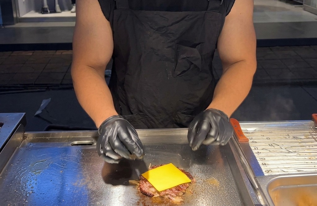 A square slice of yellow American cheese placed on top of a hot beef patty on a griddle.