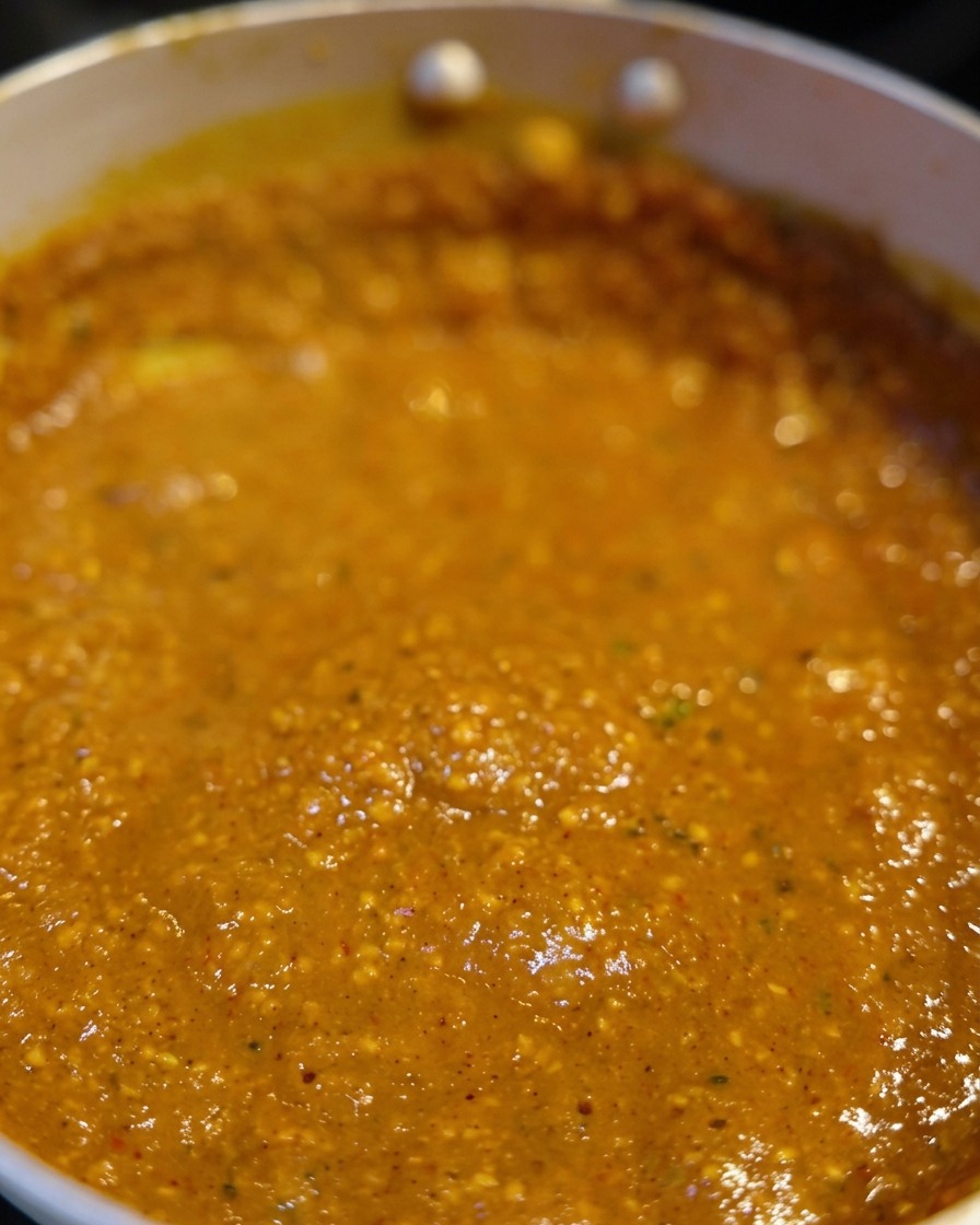 A close-up of a thick, reddish-orange miso broth bubbling in a pan.