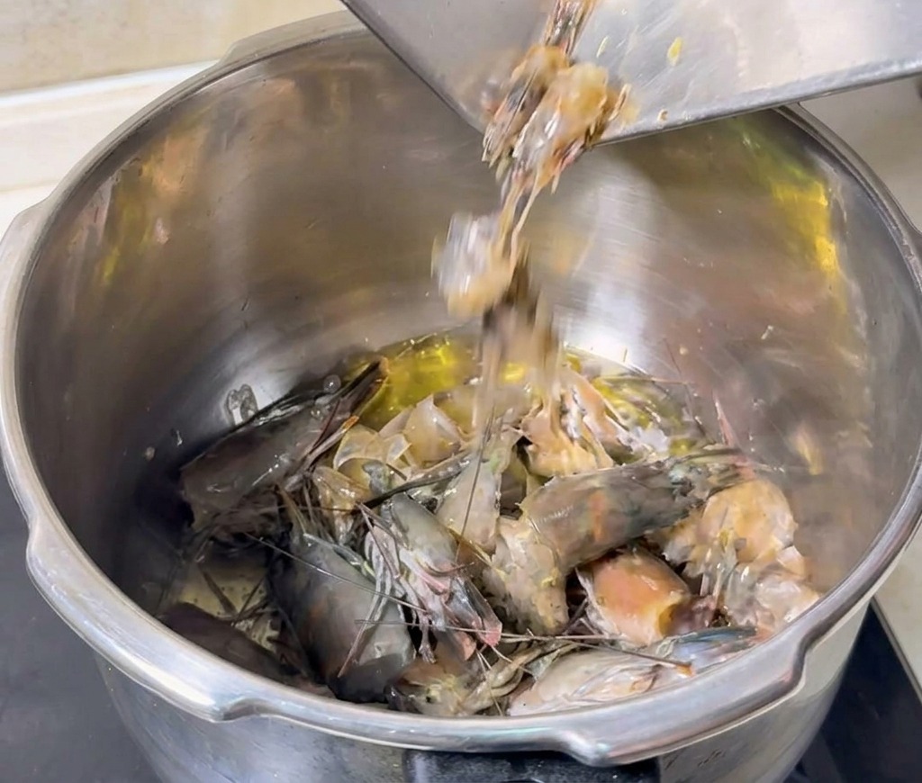 Grey shrimp heads and shells being poured from a metal tray into a pot of hot oil to be fried.