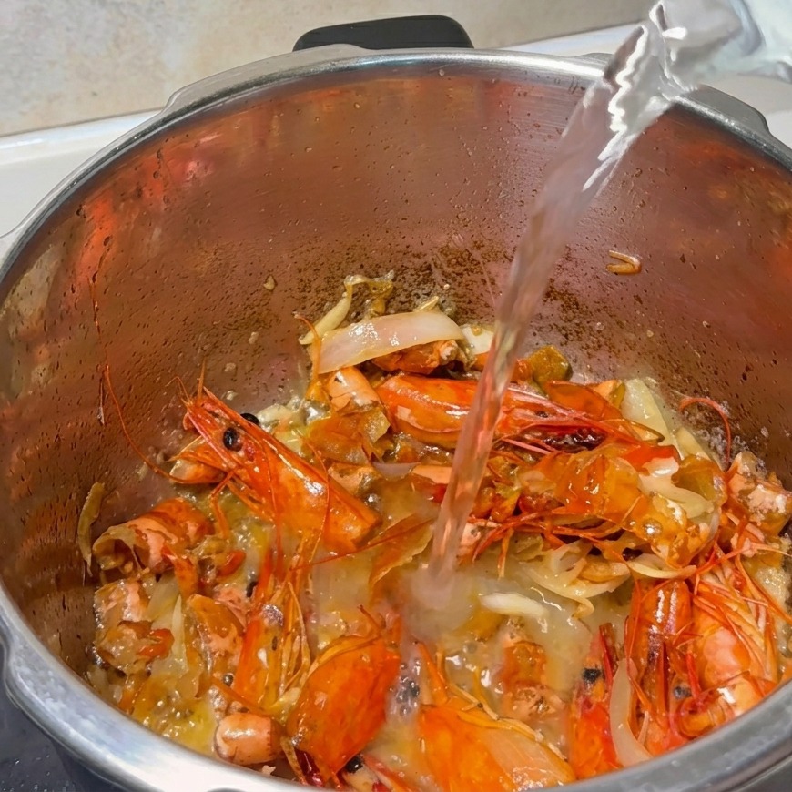A stream of water being poured into a pot filled with fried shrimp shells and sautéed aromatics.