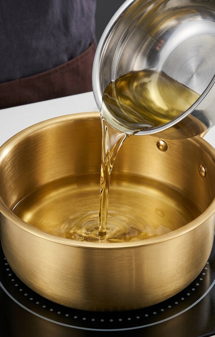 Peanut oil and sesame oil being heated in a large golden cooking pot on an induction stove.