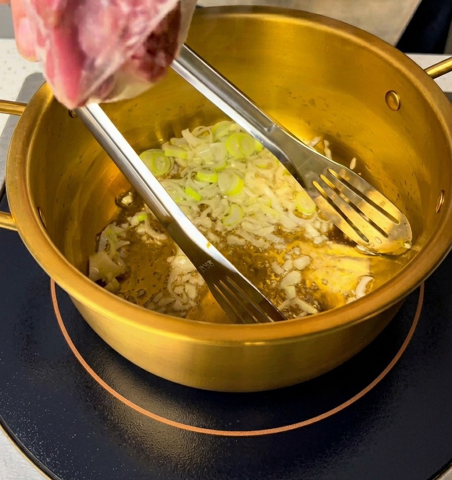 Sliced green scallions and minced garlic being sautéed in oil at the bottom of a golden pot.