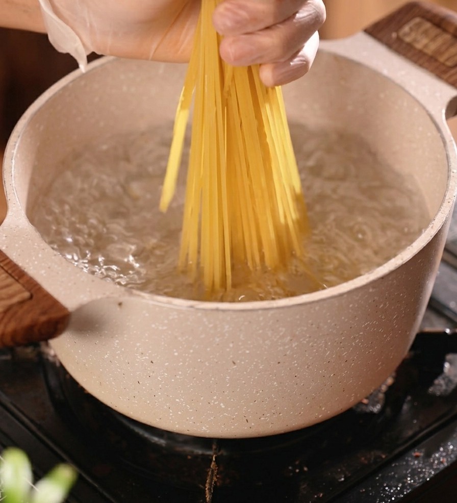 A bunch of dry spaghetti being placed into a pot of boiling water to cook.