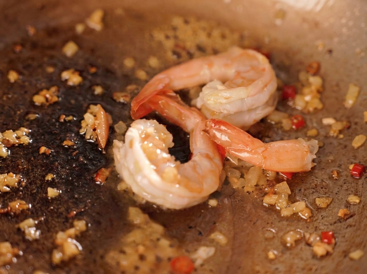 Shrimp being stir fried in a pan with chopped chili onion and yellow salted egg yolk crumbles.