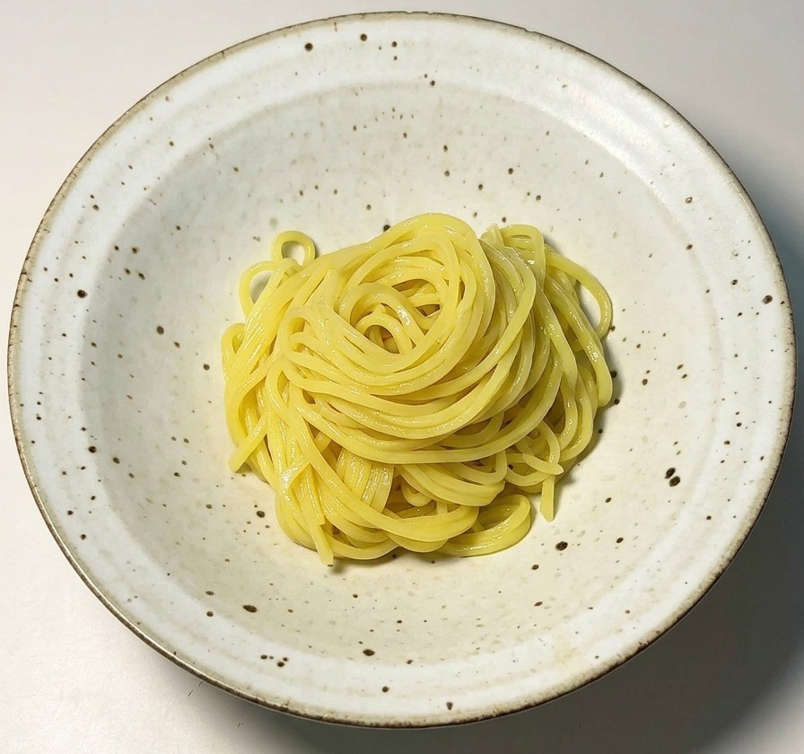 A neat bundle of yellow ramen noodles centered in a speckled white ceramic bowl.