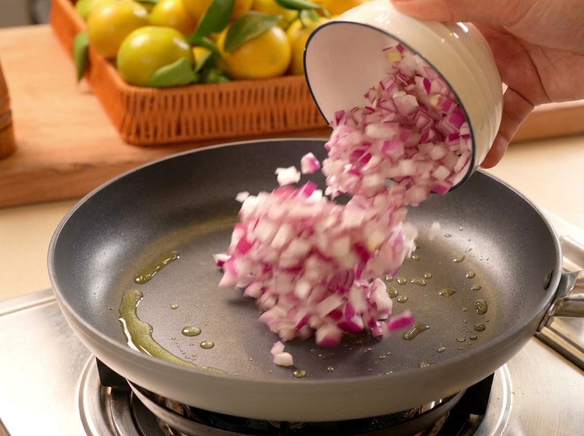 Chopped red onions being poured from a small white bowl into a heated frying pan with oil.