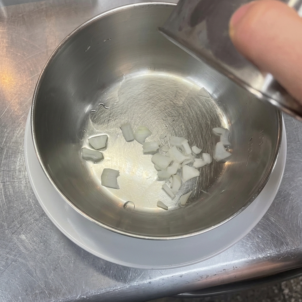 Small pieces of diced white onion sitting in the bottom of a clean stainless steel mixing bowl.