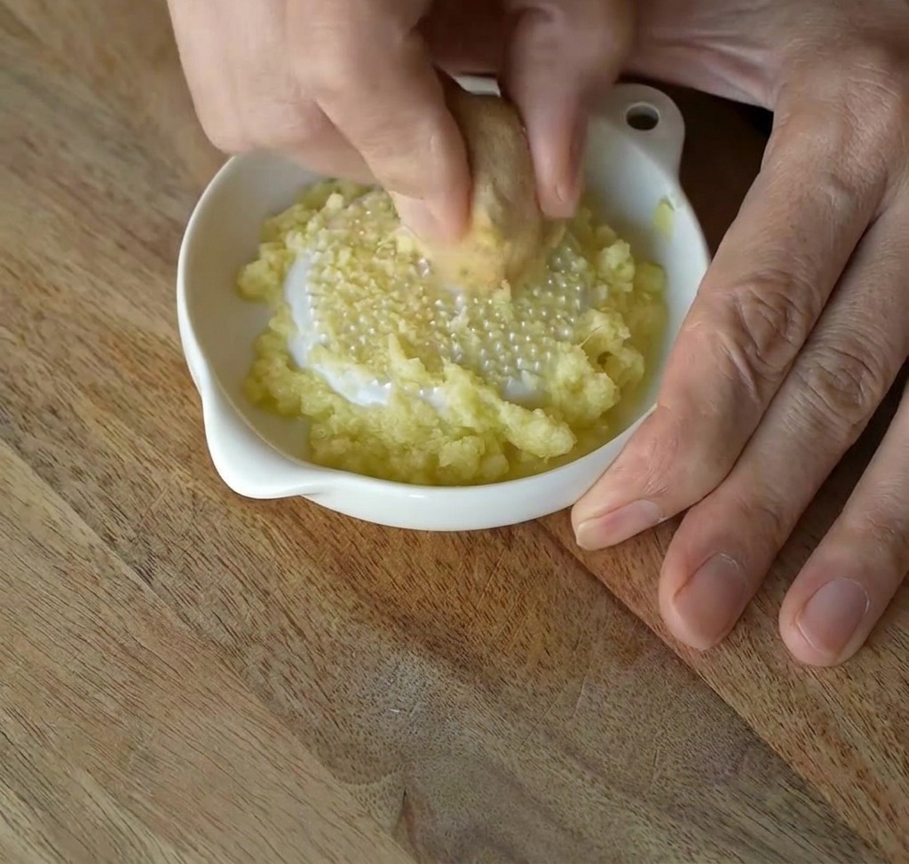 Fresh ginger being rubbed against a white ceramic grater to create a fine paste.