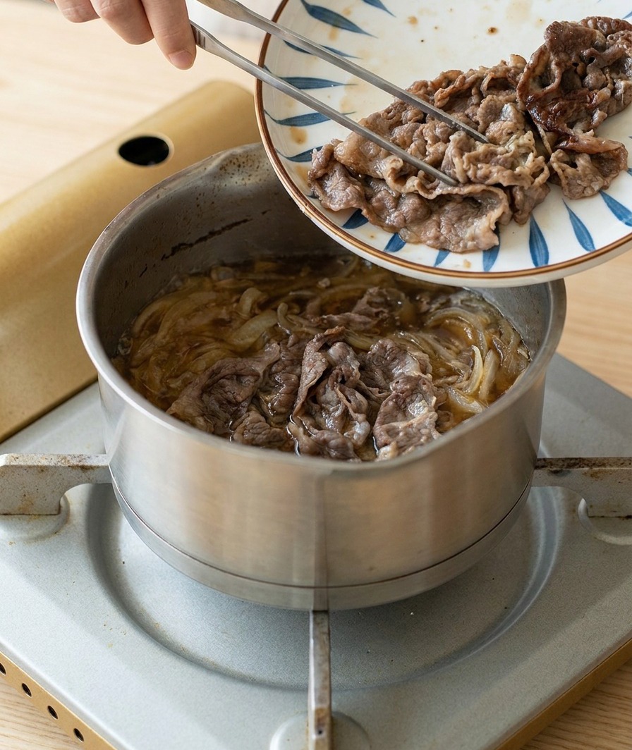 Slices of browned, seared beef being transferred from a patterned plate into a pot of simmering onions and sauce.