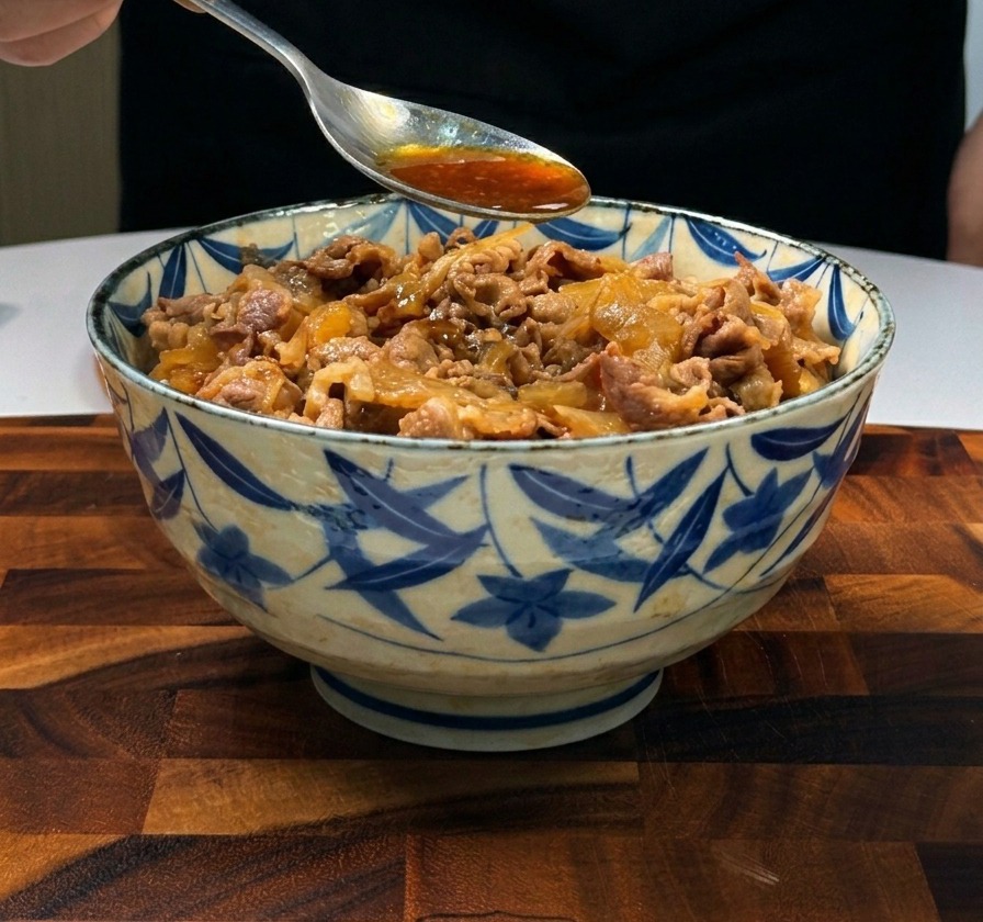 A metal spoon pouring dark brown savory sauce over thinly sliced beef and onions served on white rice.