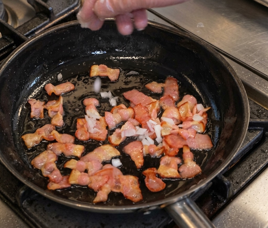Hand adding diced onions to a pan of frying bacon.