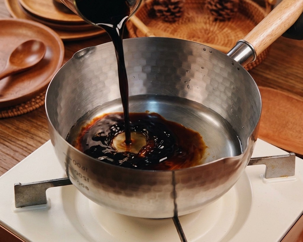 Dark soy sauce being poured into a Yukihira pot already containing water and other clear liquids.