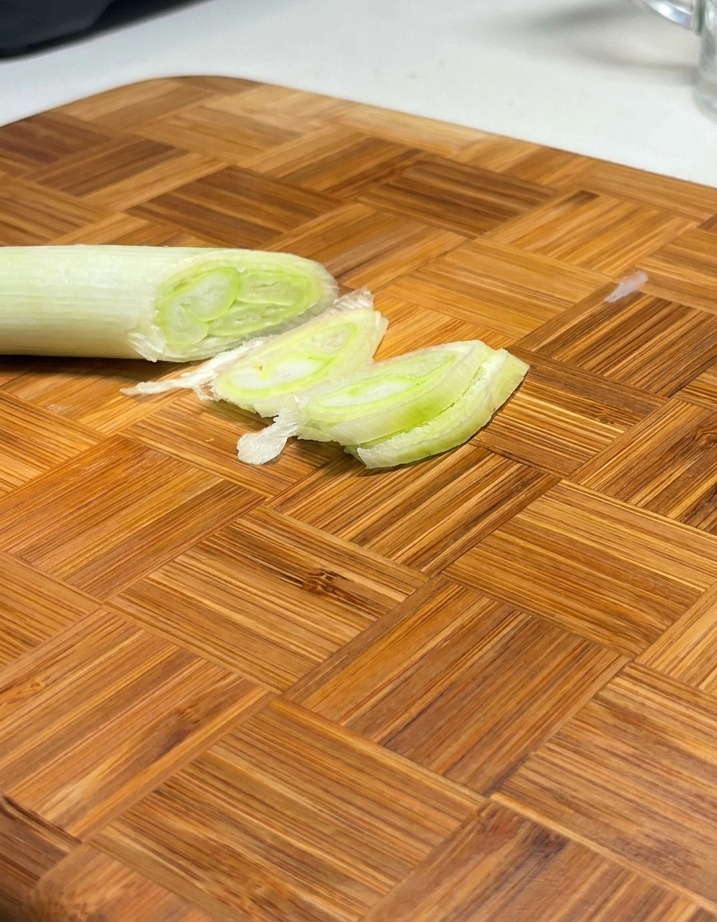 Diagonally sliced green scallions arranged on a wooden cutting board.