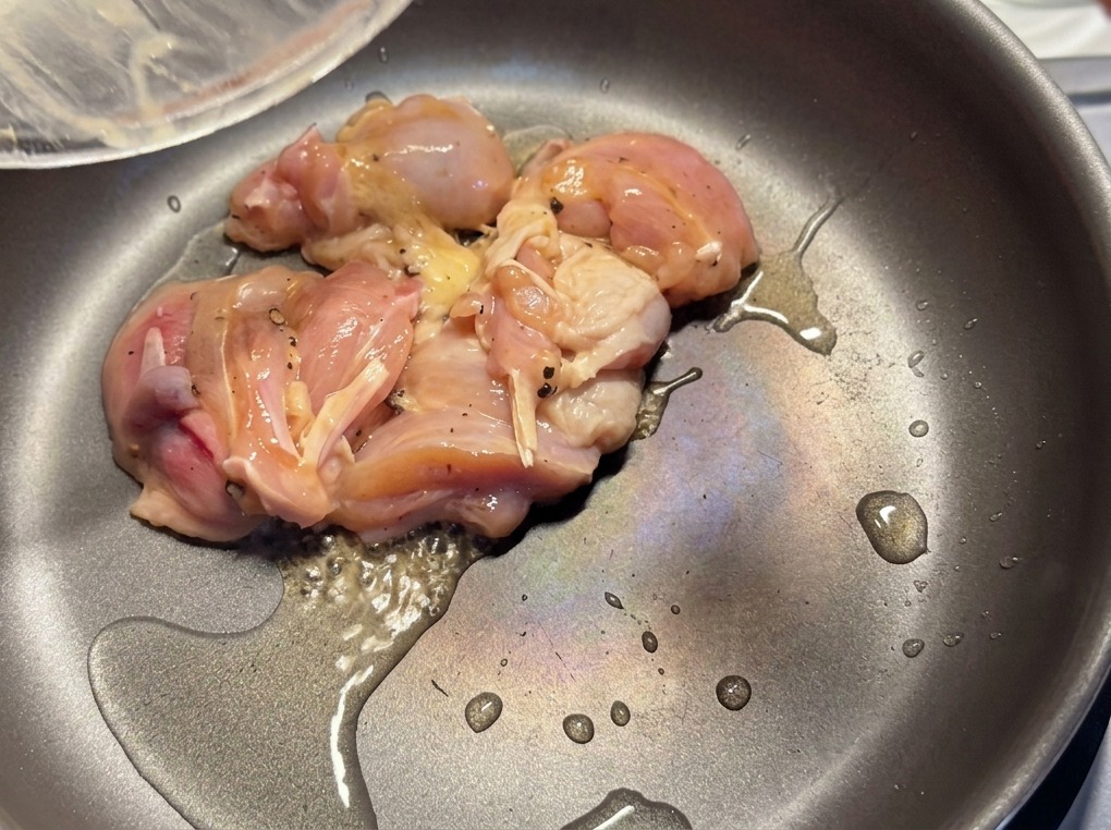 Marinated chicken pieces being seared in a hot frying pan with a light coating of oil.