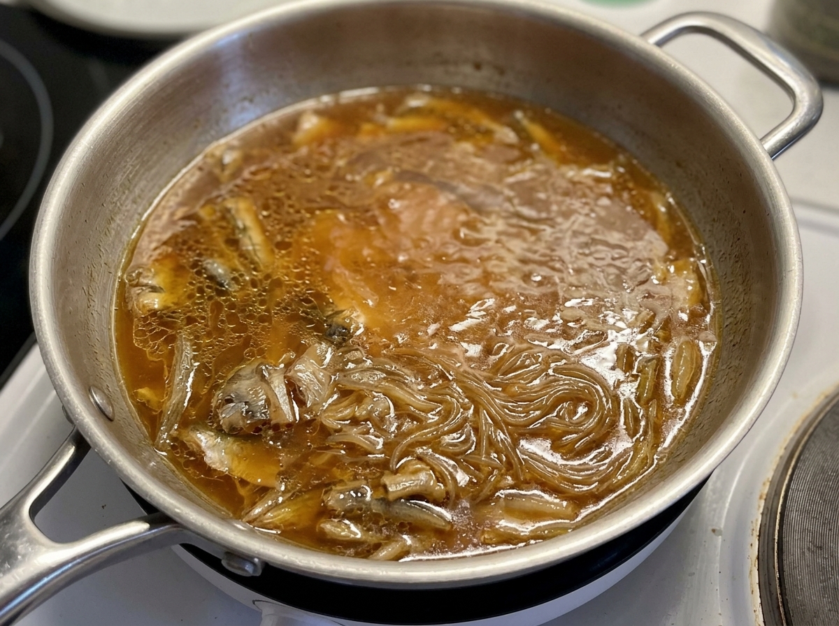 A glass lid being held over a pan where chicken and onions are simmering in a savory brown sauce.