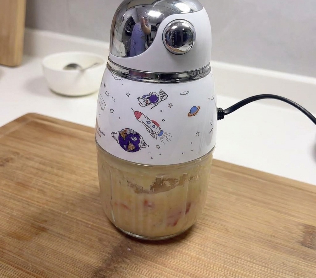 A small electric blender with space-themed illustrations containing a thick paste of blended garlic and red chilies.