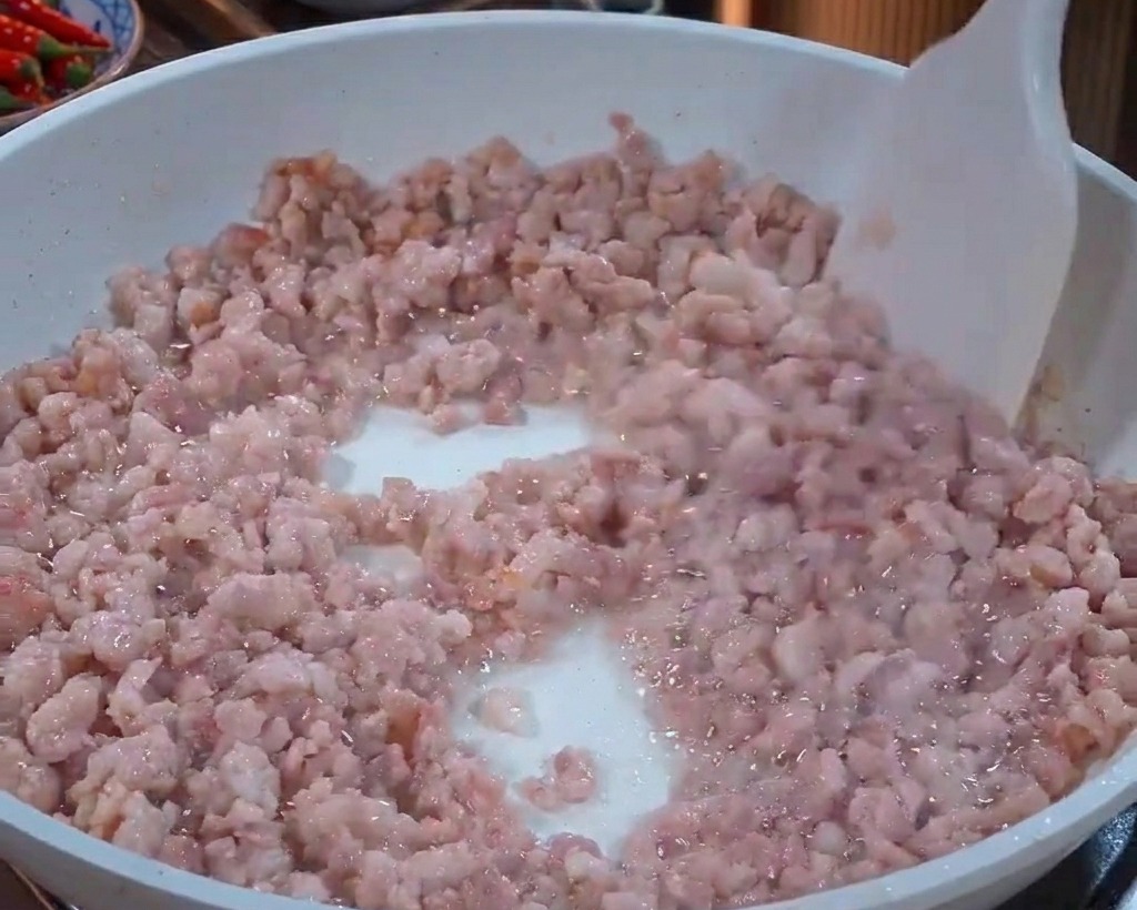 Ground pork being stirred in a white pan with a white spatula as the meat turns from pink to light grey.