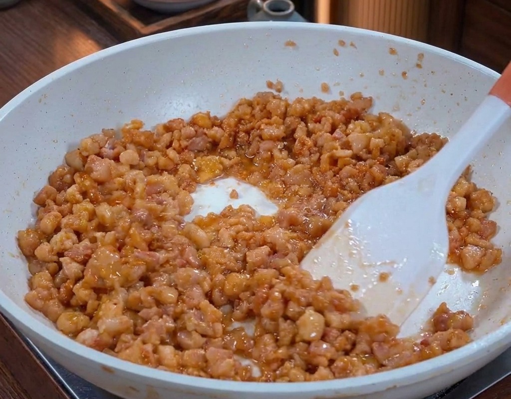 Cooked minced pork in a pan, glistening with rendered fat and appearing deeply caramelized and brown.