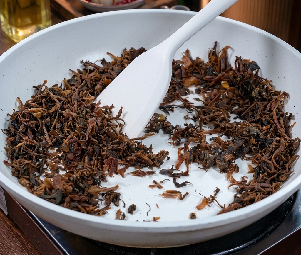 Dark brown chopped mustard greens being stirred in a white ceramic-coated pan with a white spatula.