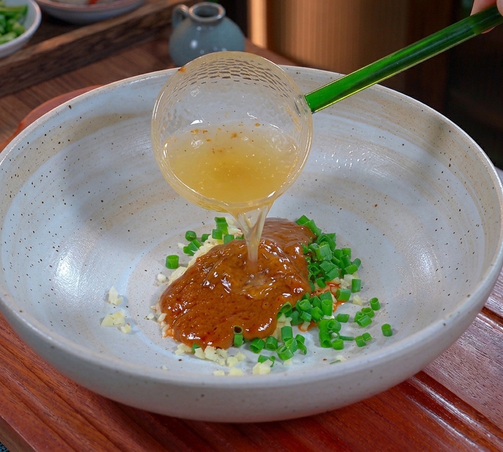 Liquid golden pork fat being poured from a translucent green ladle into a seasoning bowl.
