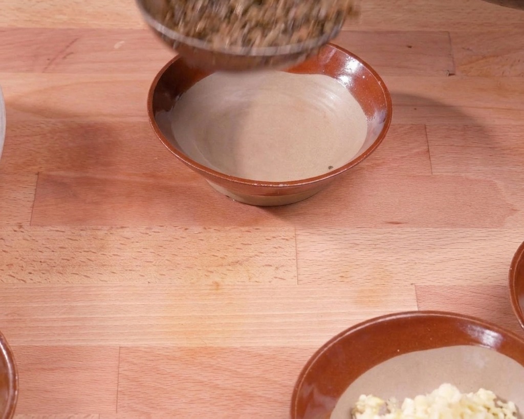 A ladle transferring the cooked pork and vegetable mixture into a brown ceramic bowl on a wooden surface.