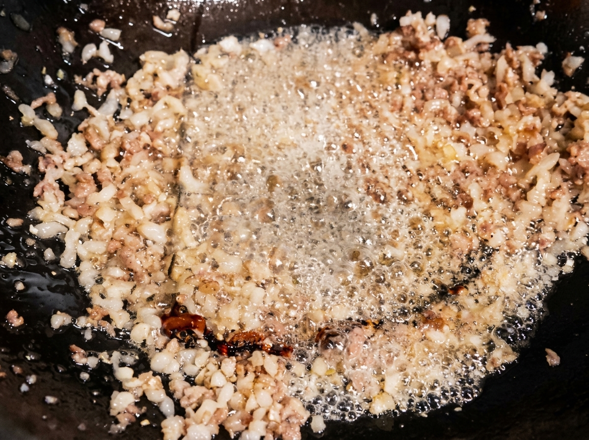 Light soy sauce being poured into a wok of stir-frying minced meat, with the seasoning bubbling in the hot oil.