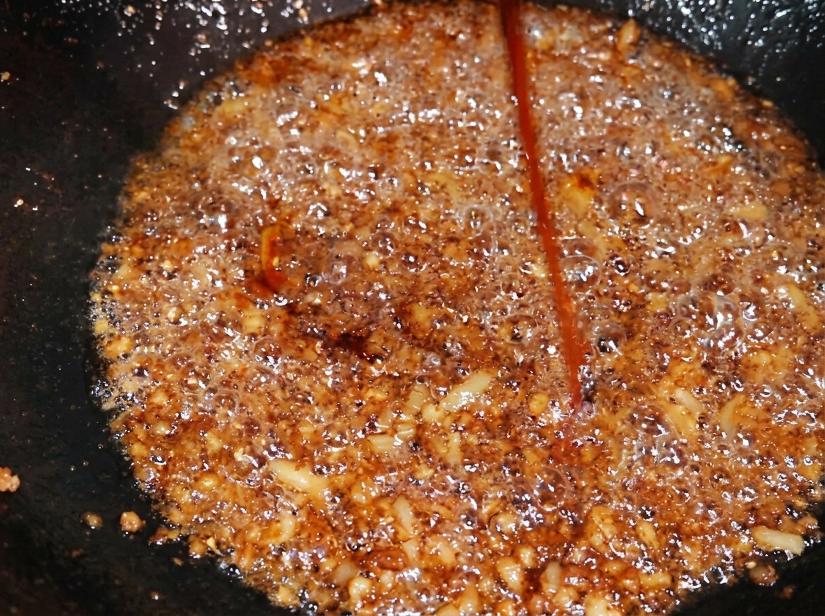 A stream of dark caramel seasoning being added to seasoned minced pork in a wok, deepening its overall color.