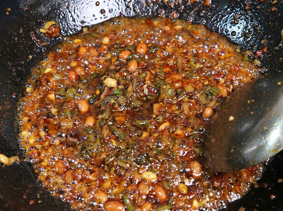 A mixture of seasoned minced pork and dark Yibin sprout vegetables being stir-fried together in a hot metal wok.