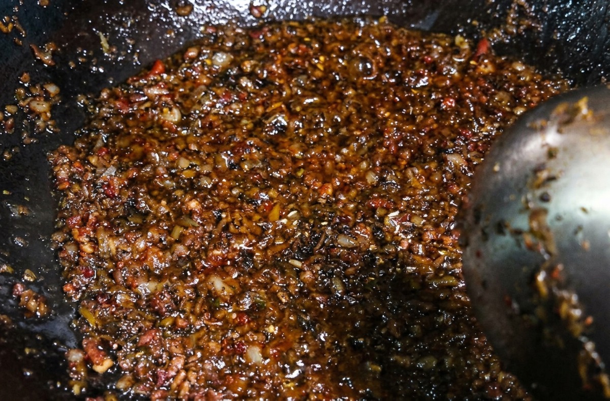 A dark, savory mixture of minced meat and sprout vegetables being stirred with a ladle in a wok after seasonings have been added.