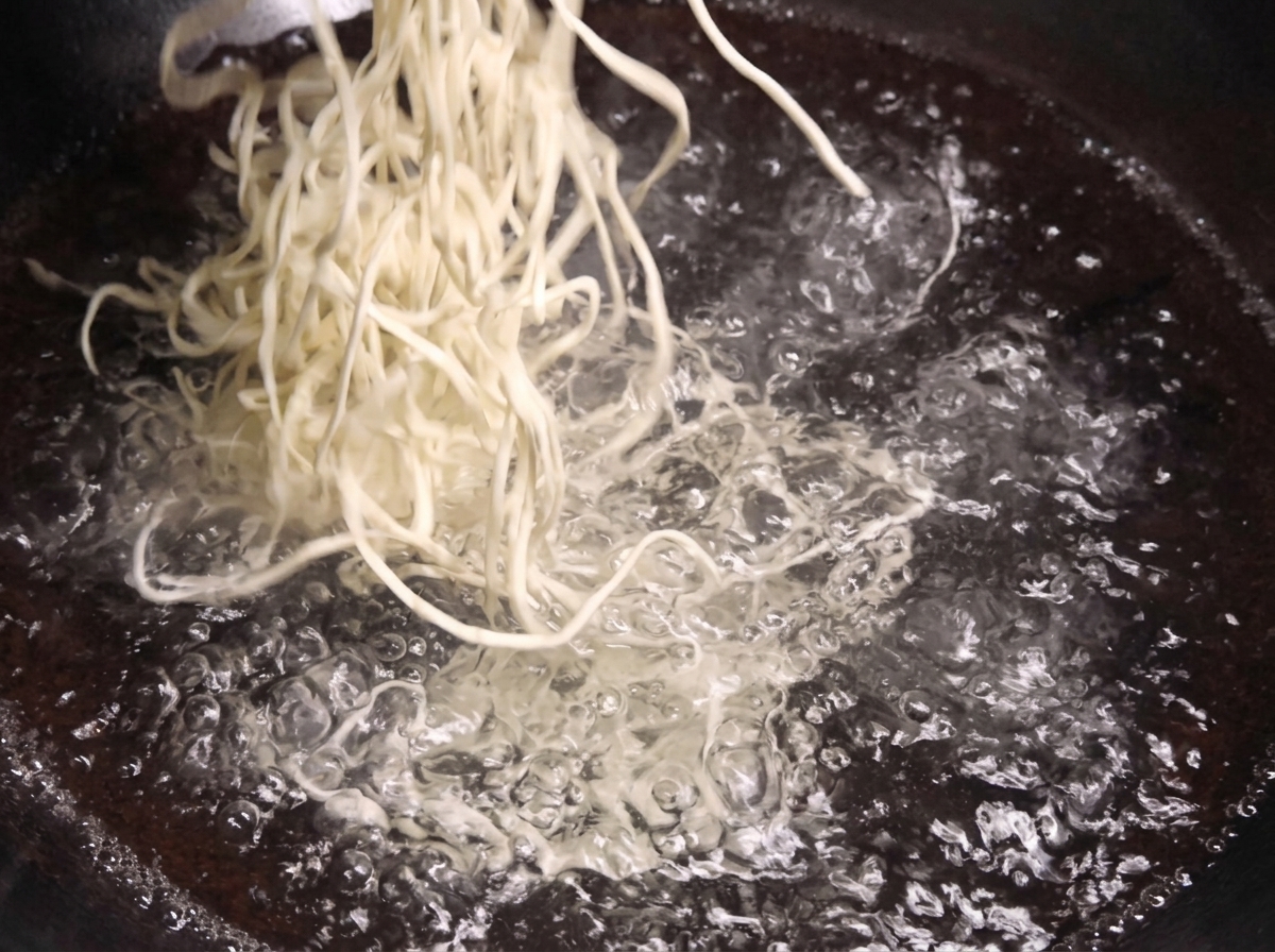 A bundle of fresh white noodles being lowered into a pot of vigorously bubbling boiling water.